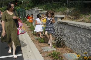 Lizzie Swaile, 7, of Bedford, under the watchful eye of mother Christina Swaile, hops from letter to letter as she travels the path of the Alphabet Garden, where each letter of the alphabet has a flower which begins with that letter at the Children's Garden at the Bedford Public Library in Temperance, Mich.