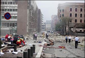 Rescue workers huddle over victims outside government offices in the center of Oslo after an explosion left a square littered with twisted metal, shattered glass, and documents that were blown out of the badly damaged buildings.