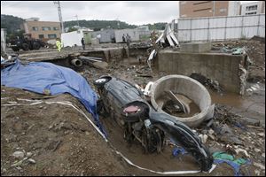 A wrecked car is left in mud Thursday after it was washed away by heavy rain in Seoul, South Korea.