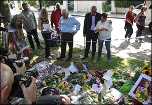 Mitch Winehouse, center blue shirt, Amy Winehouse 's father, accompanied by Janis, Amy's mother, seen right white shirt and other friends, looks at flowers placed by mourners in Camden Square outside the house of Amy Winehouse following her death, in Camden, northern London, Monday July 25, 2011.