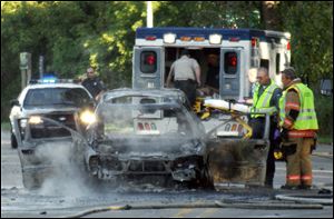 In this Tuesday, Sept. 20, 2011 photo, a Monroe firefighter sprays water on a burning car on Elm Street in Monroe, Mich.