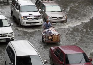 Motorists and a man pushing a cart make their way through a flooded street caused by heavy overnight rain Saturday in Bangkok, Thailand. 