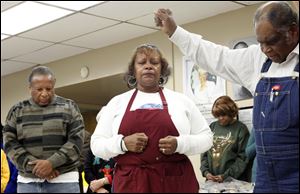 Harvey Savage, Jr., left, and Henrietta Armstrong, siblings of the kitchen's late leader, Juanita Person, pray with Leonard Mosley.