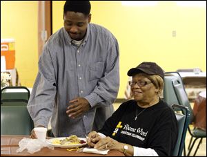Dwight Carroll Jr., left, brings a beverage to Addie Davis, 84, right, who finally sat down to eat dinner after cooking through out the day and night during the first annual Thanksgiving Dinner at the Rhema Word Christian Fellowship.