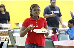 Kayla McCraney, 12, smiles after taking a bite of turkey while walking over to join a her family during the first annual Thanksgiving Dinner at the Rhema Word Christian Fellowship.