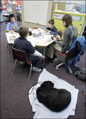 Student teacher Jenna Karg, a junior at Bowling Green State University, works in Perrysburg with Frank Elementary School students, clockwise from lower left, Justin Rader, 8, Mason McLaughlin, 10, and Ben Evans, 8, as Ms. Karg’s guide dog, Bilko, waits.