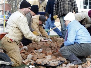 Chris Babione, left, and Kathy Zellner, right, are among the people bundled up against the cold on Wednesday as they dig through a pile of bricks after excavators dumped them over the construction fence. 