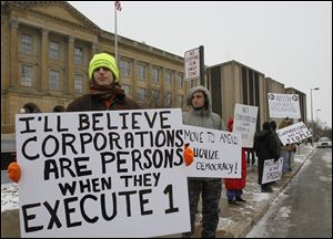 About two dozen protesters including Richard Vibbard of Walbridge, left, and Nicholas Botek of Toledo rally outside the federal courthouse in Toledo to mark the one-year anniversary of the U.S. Supreme Court ruling in Citizens United vs. the Federal Election Commission. The ‘Occupy the Courts’ rally Friday was organized in opposition to the ruling that, in effect, said corporations have the same rights as private citizens regarding contributions to election campaigns.