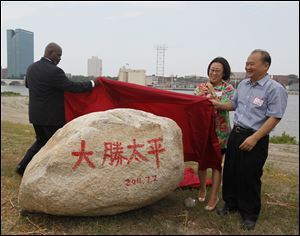 Mayor Mike Bell, Yuan Xiaohong, and Wu Kin Hung unveil a symbolic rock at a July, 2011, event marking the Chinese investors’ purchase of 69 acres of Marina District land in East Toledo. The rock, adorned with the Chinese characters for their company, Dashing Pacific, symbolizes steadiness, Mr. Wu said through a translator.