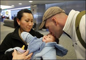 Kevin Johnson, 29, a 2000 Springfield High School alumnus with his wife Hanh Nguyen, kisses his 3-month-old son Jaxon, at Detroit Metro Airport, Feb. 14. 