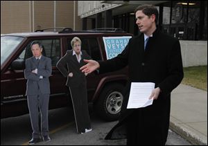 Graham Veysey campaigns in front of the main U.S. Post office in Toledo with cutouts of his opponents, Dennis Kucinich and Marcy Kaptur, behind him.