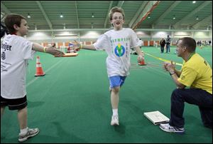 Runner Dale Domer, 10, is welcomed to the finish line for the obstacle course at the Wood County Youth Olympics by Nate Fisher, left, and team leader Brian Laux.  Teams are formed with students who are unlikely to know each other before the day's events.