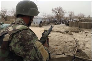 An Afghan soldier is seen in a guard tower at a military base as civilians gather outside in Panjwai, Kandahar province south of Kabul, Afghanistan. Afghan President Hamid Karzai says a U.S. service member has killed more than a dozen people in a shooting including nine children and three women. 