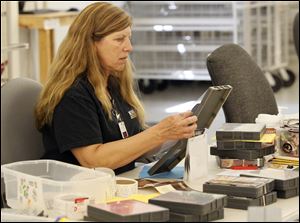 Kathy Woodbury puts stickers on CDs that are being repacked into sturdier cases so that the material inside lasts longer. 