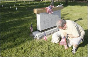 Gary Wirzylo, of Toledo, places flags at the sign for the unknown veterans in the field. 