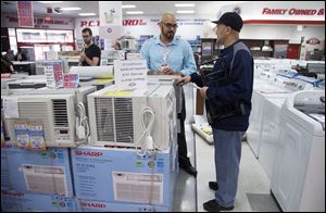 Salesman Carlos Burgos, center, helps customer Raven Campbell, right, select an air conditioner.