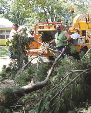 Workers Dave Tillman, left, Floyd Mitchell III, and Robert Swartz load branches felled by the July 5 storm into a chipper as Springfield Township continues its cleanup efforts.