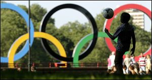 A boy plays soccer at Battersea Park while a set of Olympic rings located on a barge floats in the River Thames in the distance Sunday  in London. The city will host the 2012 London Olympics which opens Friday. When London was awarded the 2012 Summer Olympics seven years ago, officials promised they would get 2 million more people physically active in time for the opening ceremonies. But when the torch is lit July 27, the government will not only have failed, it will have backed away from its pledge entirely.