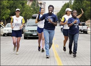 A 10,000-mile global relay passes through Toledo. It’s the 2012 World Harmony Run, whose purpose is to advance international friendship and understanding. The runners carry a flaming torch
as they travel through more than 100 nations around the globe, visiting schools along the way. From left, Rupasi Young of Seattle, Katya Pezcheklii of Ukraine, torch carrier Shunquez Spears of Toledo, Harita Davis of New Zealand, and Kyrha Benson of Toledo arrive at Toledo Farmers’ Market Saturday. The Toledoans are members of the group Safe Communities Project.