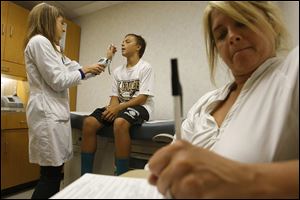 Mary Hull, left, examines Blake Howard, 12, as his mother, Monique Howard, fills out forms. Blake went to the clinic to get a physical for football, and the visit cost $49. The doctor's office would have charged $150 because insurance wouldn't have covered it.