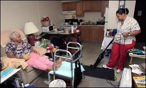 Taura Tate, right, a home care aide since 1999, vacuums as Crell Johnson, 76, looks on at Johnson's apartment in Euclid, Ohio. For the past three years, she has spent four hours each weekday morning caring for Johnson, who suffered a stroke and has diabetes. Tate cooks Johnson's oatmeal for breakfast, helps her shower and watches to make sure she takes the right medicine.