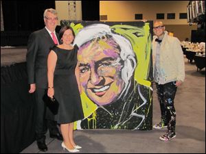 Arnaud de Weert and Yolanda Jimenez purchased this Jamie Farr portrait which was painted by artist David Garibaldi, standing with them.