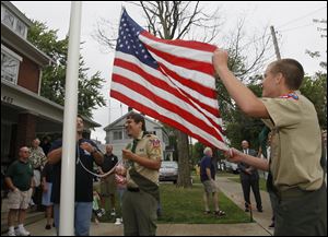Open Door Ministries' Collin Cogswell, partly obscured by the flagpole, Robert Lagger, center, and fellow Troop 210 member Adam Chamberlain raise the flag on the front lawn of the home in East Toledo.