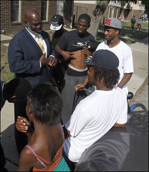 Mayor Mike Bell speaks to local youths before the start of a prayer vigil for two children who were recently shot in a Moody Manor apartment in Toledo, Ohio. Tyrell James, 18, lifts his shirt to show the mayor where he was once shot. DeAngelo Gott, 18, leaning against the car, was previously shot 4 times.