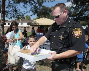 Lucas County Sheriff's Deputy Corey Cole hands a coloring book to Corey Colbert, 8, while Victoria Herman, left, juggles items for her daughter. They were among the crowd at Birmingham Terrace in East Toledo on Saturday afternoon.