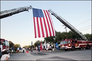 Two Toledo Fire Department ladder trucks provide an archway to mark the start line of the 5K run and support an American flag flown in honor of Navy Week festivities in Toledo.