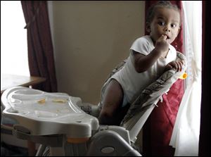 Eli James, 1, peeks out the window from his high chair in his Platt Street home. He was just an infant when older brother Lawrence James, 19, was shot by home intruders.