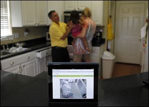 A webcam feed is shown on an iPad of four-month-old Emily St. Martin in the Neonatal Intensive Care Unit at Ochsner Medical Center, at her family's home in LaPlace, La. Her parents, Laura and David St. Martin, with their daughter Jacqueline, 2, background, are able to watch her from a web cam installed over her crib on their iPad.