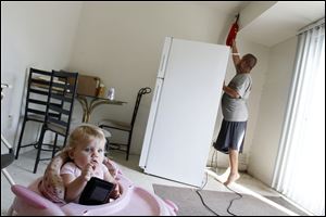 Robert Ault uses a vacuum to get rid of bugs as his daughter Destiny Ault, 23 months old, sits in a walker in the apartment of Robert Alt at Greenbelt Apartments.