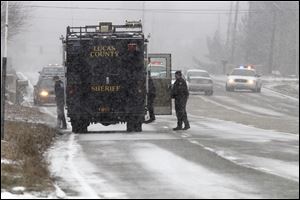 Emergency responders wait near 8000 Airport Highway, where an armed man has barricaded himself in a house.