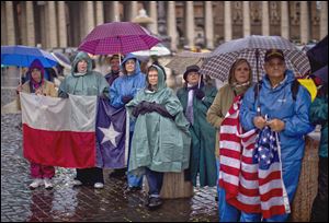 A group waiting in St. Peter's Square holds U.S. and Texas flags while watching a video monitor during the first day of voting for a new pope. 