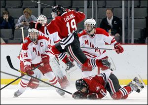 St. Cloud State's Drew LeBlanc (19) hurdles teammate Kalle Kossila (11) as he chases after the puck.