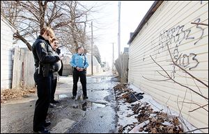 Toledo Police Officers Denise Fischer, left, and J.C. Eischen, right, speak with David Corns, a homeowner in the 600 block of East Broadway who had alerted  authorities to the gang-related graffiti on the back of his garage.