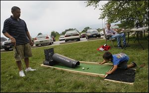 Robert Torres, left, watches as Gavin Mejia, 2, of Fremont, tries his hand at golf. The game was one of many activities offered. Live music by local bands and theater performances also were part of the mix.