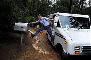 Dave Jackson closes a mailbox with his foot after delivering the mail Friday to a home surrounded on three sides by a flooded Cheyenne Creek.