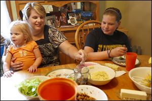 Jodie Banaszak helps her daughter Mackenzie, 2, left, eat while talking with her daughter Cassidy, 10, right, over dinner in their home in Toledo. Jodie has lost 50 pounds since undergoing surgery for a gastric sleeve, which reduced the size of her stomach by 90 percent, two months ago. 