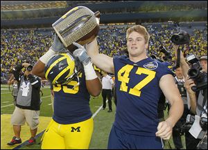 Wolverines Jibreel Black (55) and Jake Ryan (47) carry the Little Brown Jug off the field after beating the University of Minnesota on Saturday. Ondre Pipkins suffered a torn ACL in the game.