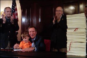 Felix Falco Plouck, 4, the son of a Cabinet member, helps Ohio Gov. John Kasich sign the state's $62 billion, two-year budget on June 30 in Columbus, Ohio. Kasich is flanked by, state Sen. Keith Faber, left, and House Finance Chairman Ron Amstutz, right.