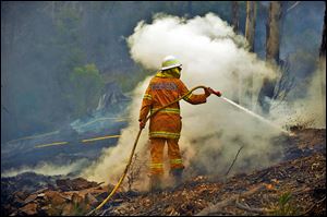 A volunteer firefighter in New South Wales puts out hot spots in the town of Bell, Australia, on Sunday. The blazes are exacerbated by wind and high temperatures.