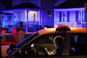A Toledo police officer records information at the scene of a slaying in North Toledo on Wednesday night. Detectives have sworn out an arrest warrant for a man they believe is a suspect in the fatal shooting in the 600 block of Spring Street.