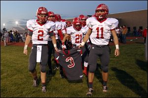 Bedford senior quarterback Brad Boss (2) and senior Alec Hullibarger (11) carry the jersey of their teammate Colton Durbin as they lead their team onto the field at Jefferson High School in Monroe.