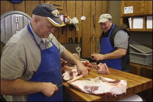 Paul De Land, left, jokes with his brother Steve De Land as they trim and cut beef behind the counter.