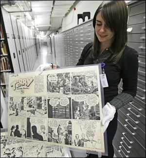 Caitlin McGurk holds up a cartoon from ‘Terry and the Pirates’ by Milton Caniff at the Billy Ireland Cartoon Library and Museum in Columbus. The museum has more than 300,000 original comic strips from such artists as Charles Schultz and Garry Trudeau.