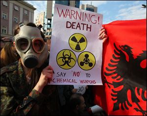 An Albanian student wears a gas mask and holds a sign  during a protest against chemical weapons during a  protest against the dismantling of Syrian chemical weapons in Albania in front of the Prime Minister's office in Tirana  Thursday.
