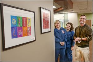 Registered nurses Kate Samberg, left, and Sarah Meiner stand with Dr. Chris Goliver near artwork done by local students in the new Mercy Emergency Services-Perrysburg. Artwork is to be rotated yearly.