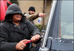 Samantha Hernandez scrapes ice off of the windows after Kenneth Fields sprays them with a concoction of vinegar and water to soften the ice on Saturday in Odessa, Texas.